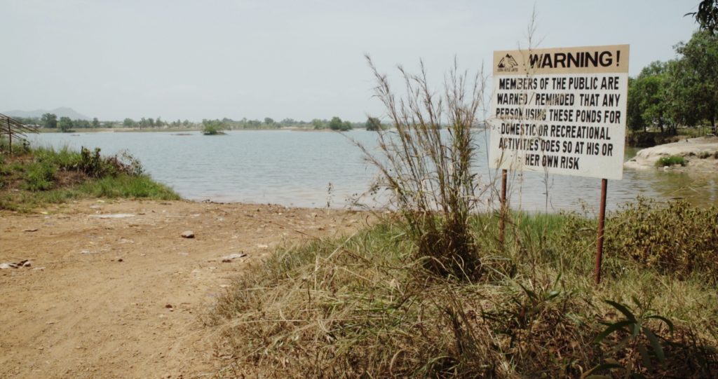 A sign by a lake warns people that they enter or use the water at their own risk