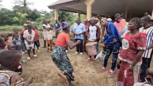Screenshot of landowners dancing and playing drums outside in village